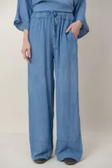 Pantalon de lino color azul, de corte ancho y relajado, con cintura elastizada ajustable mediante cordón y bolsillos laterales. Presenta detalles de alforzas en los bajos.