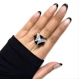 Anillo negro con base circular y aplique de mariposa blanca calada.