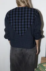 Blusa de algodón con estampado a cuadros en tonos azul y negro, con bordados decorativos en color bordó sobre el canesú. Presenta cierre frontal con botones, cuello redondo y mangas largas levemente abullonadas.