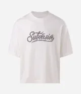 Remera boxy de algodón color blanco crudo, con cuello redondo, mangas cortas y estampa frontal en tipografía gótica con efecto de alambre de púa.