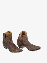 Bota corta estilo cowboy de cuero marrón desgastado, con punta afilada y tacón bajo. Presenta bordados en hilo dorado en el empeine y caña, incluyendo un diseño de estrellas troqueladas en la puntera. El tacón tiene un acabado envejecido plateado.