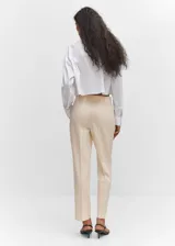 Pantalon de vestir de corte recto y tiro medio, confeccionado en tejido fluido color beige. Presenta trabillas en la cintura, dos bolsillos laterales y dos bolsillos de ribete en la parte posterior.