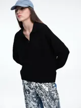 Sweater de tejido de punto color beige, con diseño de trenzas en el frente y mangas lisas. Presenta cuello polo con escote en V y puños y ruedo acanalados.