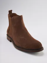 Bota Chelsea de gamuza gris con elásticos laterales, suela de goma marrón y tirador trasero.