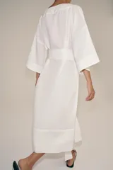 Vestido tipo túnica de corte evasé, color blanco, con escote en pico, mangas por debajo del codo y cinturón ajustable del mismo tejido.