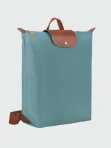 Mochila de diseño minimalista en color beige, con solapa y asa superior en cuero marrón texturizado. Cuenta con correas ajustables en color marrón y cierre principal.