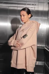 Buzo oversize color nude confeccionado en frisa, con capucha amplia, bolsillo canguro, terminaciones de puño y ruedo con rib, y logo de la marca bordado en el centro delantero.