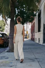 Pantalón de tiro medio, pierna ancha, confeccionado en tejido texturado de color claro con hilo metalizado. Presenta falsos bolsillos delanteros con botones metálicos dorados.