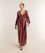 Vestido largo evasé de Marfinno, confeccionado en mezcla de viscosa y lino, con diseño de rayas verticales en tonos bordó y beige. Presenta escote en V, busto ajustado y mangas largas abullonadas con puños elastizados.