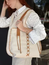 Bolso tipo tote de cuero color crudo con costuras decorativas en hilo color cuero. Tiene doble asa de cuero color cuero y forro interior de tela.