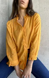 Camisa color mostaza con bordado de flores, cuello con volados, mangas largas abullonadas y cierre frontal con botones.