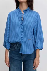 Camisa de manga larga con diseño a rayas verticales en tonos azules. Presenta un cuello mao con detalle de volados a lo largo de la abertura frontal y mangas abullonadas con puños elásticos.