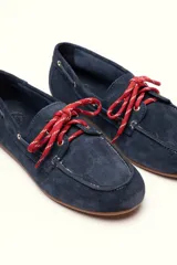 Mocasín tipo boat shoe color marrón, confeccionado en cuero, con cordones de cuero marrón y cordones decorativos azules.
