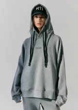 Buzo gris de frisa con capucha, bolsillos delanteros y corte oversize. Tiene recortes laterales, doble cordón con puntera de goma y estampa en frente y espalda.