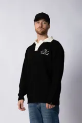 Sweater de punto con textura waffle en color blanco, con cuello polo en contraste color verde oscuro y cierre frontal de botones. Presenta un bordado decorativo en el pecho y un corte relajado.