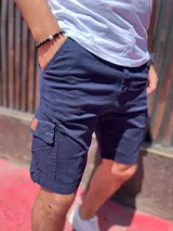 Bermuda cargo de gabardina en color azul marino, con bolsillos laterales con solapa y detalle de etiqueta de cuero sintético.