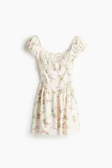 Vestido corto de popelina de algodón, color blanco con estampado floreado en tonos rosados y verdes, escote cuadrado con cordón ajustable, mangas cortas abullonadas y pollera acampanada.