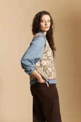 Chaleco tejido de corte recto y sin mangas, con diseño floral ornamental en tonos beige y marrón. Presenta cierre frontal con botones y cuello redondo.