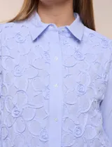 Camisa de algodón celeste con patrón de milrayas finas y aplicaciones florales en relieve deshilachado en el frente. Cuenta con cuello camisero tradicional, cierre frontal con botones, mangas largas con puños abotonados y corte semi holgado.