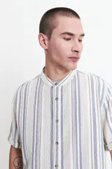 Camisa de manga corta con cuello mao y diseño a rayas verticales en tonos azules y crudo. Confeccionada en tejido de algodón con textura y corte slim fit.