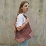 Bolso tipo hobo grande de eco cuero con textura símil gamuza color bordó, con refuerzos en la base y detalles en eco cuero marrón claro en las esquinas inferiores y tiras.