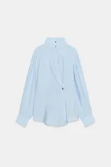 Camisa de cuello alto y manga larga, confeccionada en tejido satinado. Presenta un diseño con pliegue frontal decorativo con botón visible y cierre frontal con botones ocultos bajo solapa.