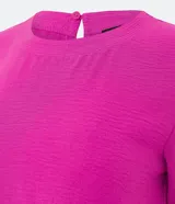 Blusa blanca de poliéster con cuello redondo, mangas cortas, cierre trasero en forma de gota, pequeñas aberturas laterales y acabados en pespuntes en las mangas y el cuello.