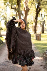 Poncho de lana merino color chocolate, con diseño sin cuello, caída fluida y flecos en el ruedo.