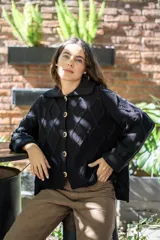 Saco tejido de punto con diseño de ochos y trenzas, color negro. Presenta cuello estilo camisero, cierre frontal con botones tipo joya, mangas holgadas y silueta oversize.