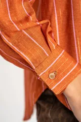 Camisa oversize color ladrillo con rayas verticales blancas y rosadas, de mangas largas y botones de madera.