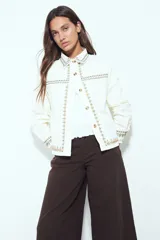 Campera de jean color blanco con bordados geométricos en cuello, delantero, bolsillos, puños y ruedo. Tiene botones dorados y un calce recto y relajado.