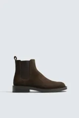 Bota estilo Chelsea con parte superior de piel con acabado en serraje, elásticos laterales para facilitar el calce, horma redonda y suela con ligero tacón.