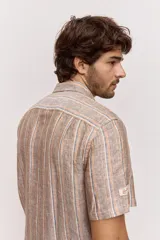 Camisa de manga corta con diseño a rayas verticales en tonos tostado, blanco y azul. Cuenta con cuello clásico y cierre frontal de botones.