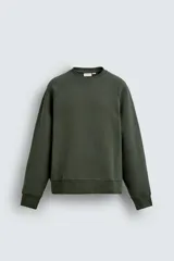 Sudadera de corte relajado con cuello redondo, confeccionada en algodón compacto con interior de rizo. Presenta mangas largas de diseño raglán y terminaciones en rib en cuello, puños y ruedo.