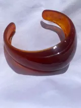 Brazalete rígido de resina en color ámbar, con diseño curvo y acabado brillante.