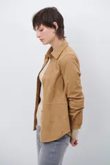 Camisa de estilo casual confeccionada en material tipo gamuza color marrón, con cuello clásico, cierre frontal con botones y costuras a la vista en tono contrastante.