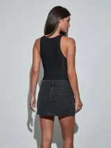Minifalda de denim gris oscuro con tachas metálicas plateadas distribuidas por toda la prenda, bolsillos delanteros y cierre de botón y cremallera.