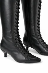 Botas altas de caña alta negras confeccionadas en PU, con diseño acordonado frontal, punta fina, cierre lateral y taco bajo fino.