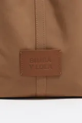 Bolso grande Bimba y Lola color marrón, con exterior de gabardina y detalles en cuero vacuno. Presenta doble asa de mano, correa ajustable, cierre con botón a presión, logo metálico de la marca en dorado y bolsillo interior con cremallera.