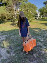 Bolso de lona fucsia combinado con detalles y asas de cuero tostado, de diseño espacioso con cierre superior y correa ajustable.
