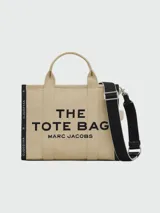 Bolso tote Marc Jacobs modelo The Jacquard, confeccionado en tejido de lona negro con detalles en blanco. Presenta el logo de la marca y la inscripción 'THE TOTE BAG' en el frente, con doble asa superior y correa ajustable extraíble.