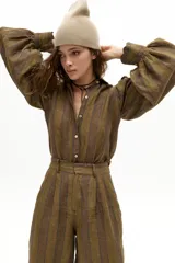 Camisa de lino con estampado de rayas verticales en tonos tierra. Presenta cuello camisero clásico, cierre frontal con botones de nácar, mangas largas abullonadas y puños con terminación ondulada.