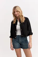 Chaqueta liviana de corte recto, color negro, con cuello camisero, cierre frontal con broches metálicos y bolsillos ribeteados.