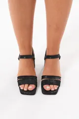 Sandalias de taco ancho color negro, con diseño de doble tira delantera, punta cuadrada y tira ajustable con hebilla en el tobillo.