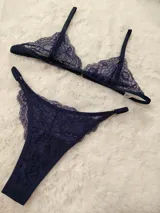 Conjunto de lencería de encaje color azul marino, compuesto por un soutien triangular sin relleno con tirantes regulables y una bombacha colaless ajustable con tiras laterales y detalles de argollas metálicas.