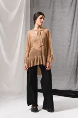 Blusa de tul beige con mangas largas abullonadas terminadas en volados, escote en V con detalle de lazo para atar al cuello y dobladillo con volados.