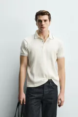 Remera polo de punto canalé color azul marino, de corte regular fit, con cuello solapa y cierre frontal de botones a presión. Cuenta con mangas cortas con ribetes blancos en los bordes del cuello y de las mangas.