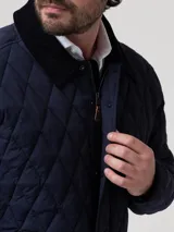 Campera acolchada azul marino con costuras en rombos, cuello de pana negro y cierre frontal con botones a presión. Incluye bolsillos laterales con ribete de pana y broches ajustables en la cintura.