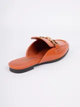 Zuecos abiertos de símil cuero color negro, con punta cuadrada, aplique metálico dorado en la parte superior y taco bajo.