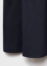 Vestido corto sin mangas con efecto denim, cuello redondo y detalle de lazos frontales. Presenta un diseño con tablas y cierre de cremallera en la parte posterior.